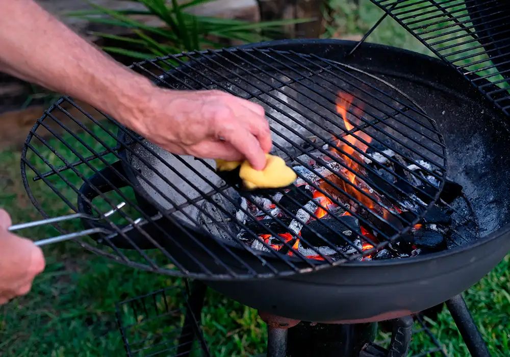 Man cleaning a barbecue grill with a sponge, while the fire is on