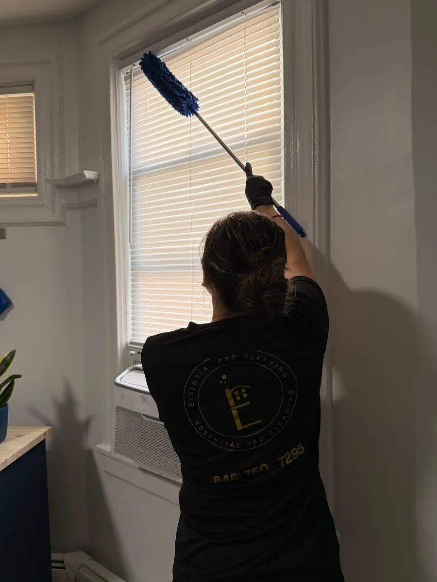 Essential Pro Cleaning team member dusting window blinds with an extendable duster